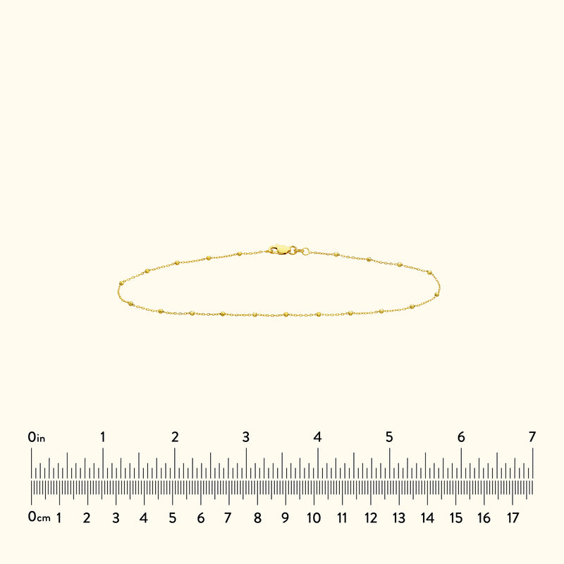 Thin gold bracelet with small decorative beads, displayed against a light background.