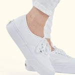 Delicate gold anklet worn above a white sneaker with a casual outfit.