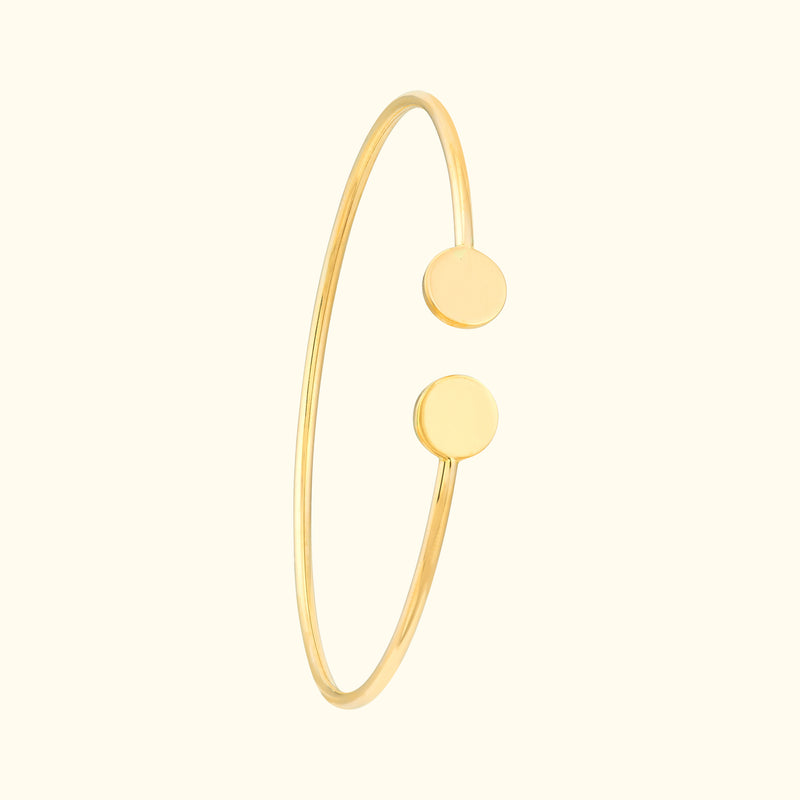 Gold bangle bracelet with two circular accents on opposite ends.