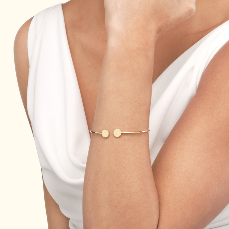 A gold bracelet with two circular accents worn on a woman's wrist.