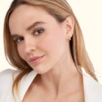 Young woman with long hair wearing gold hoop earrings, smiling softly.