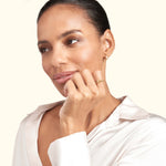 A woman wearing a simple gold ring and earrings, with a thoughtful expression.