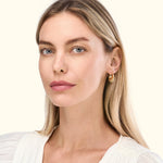 A woman with long blonde hair is wearing gold hoop earrings and a white blouse.