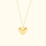 Gold heart pendant necklace on a delicate chain against a light background.