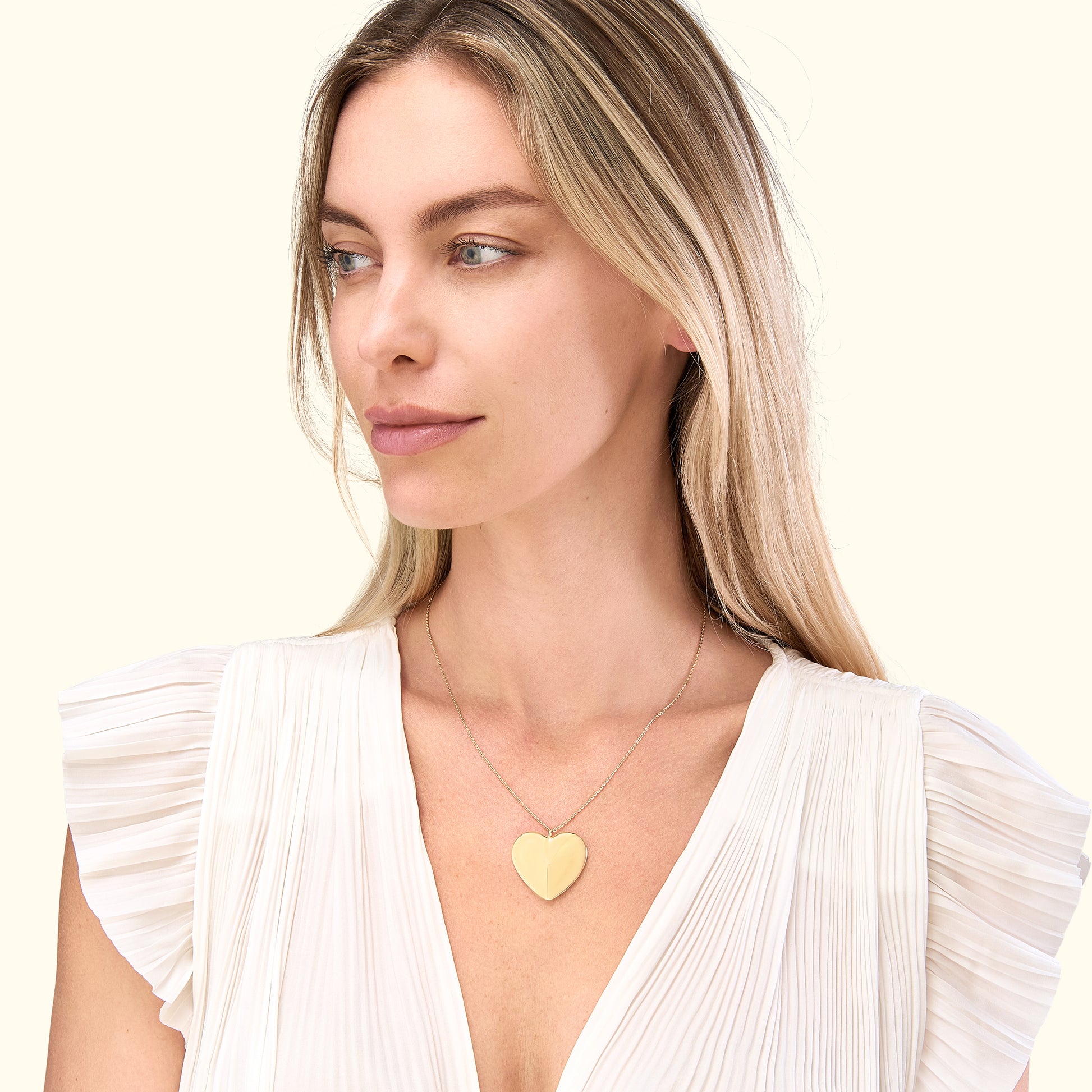 Blonde woman wearing a heart-shaped gold pendant necklace, smiling softly.