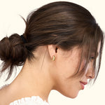 A woman in profile wears a gold earring, showcasing her elegant hairstyle and features.