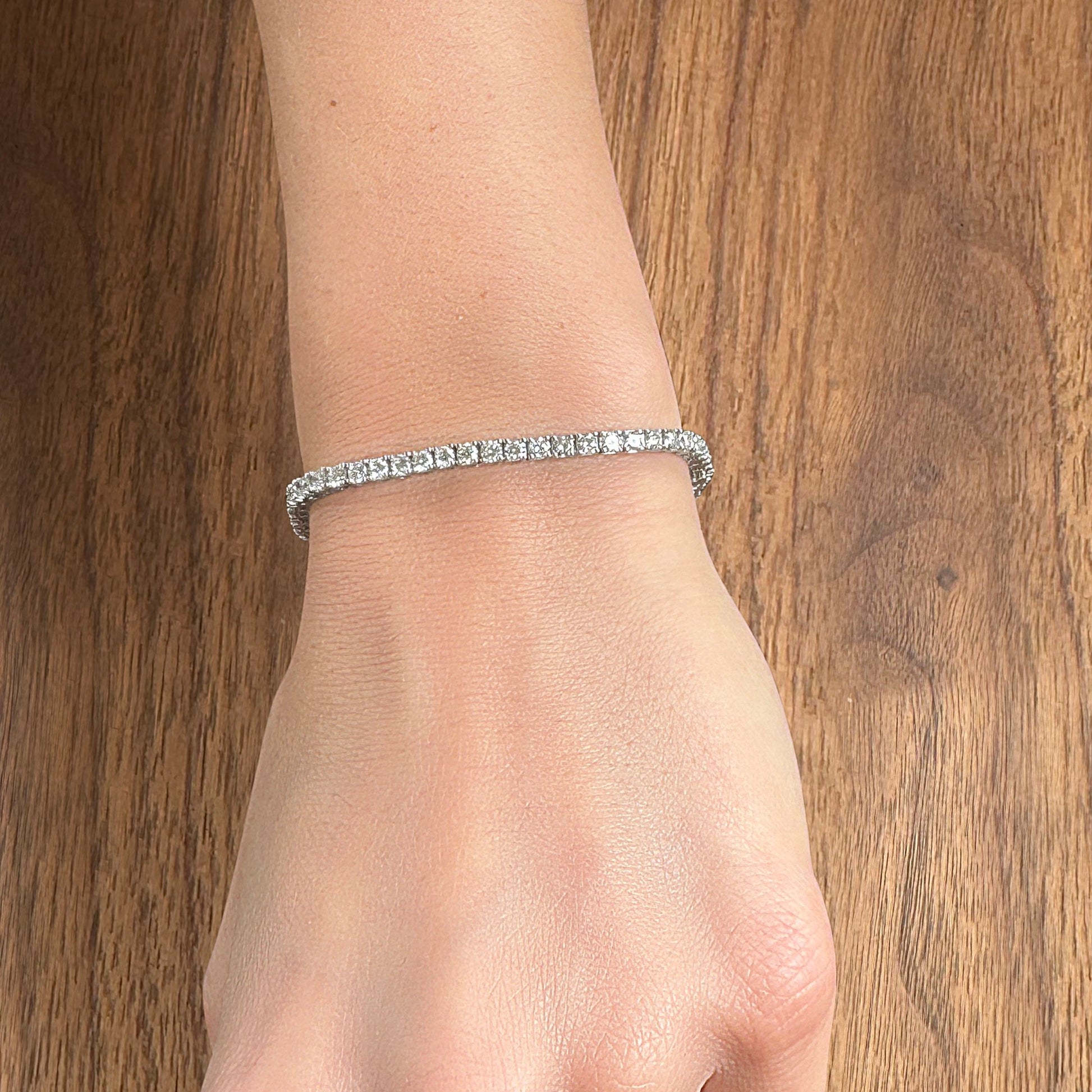 A sparkling diamond bracelet worn on a woman's wrist against a wooden background.