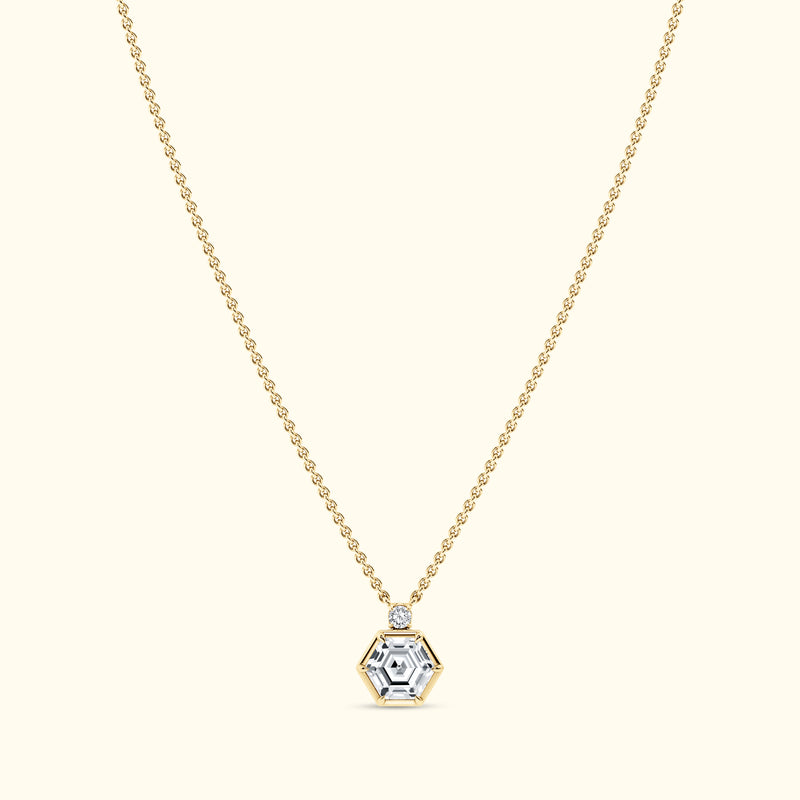 Gold necklace with a hexagonal diamond pendant on a light background.