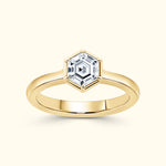 Gold ring with a hexagonal diamond centerpiece on a light background.